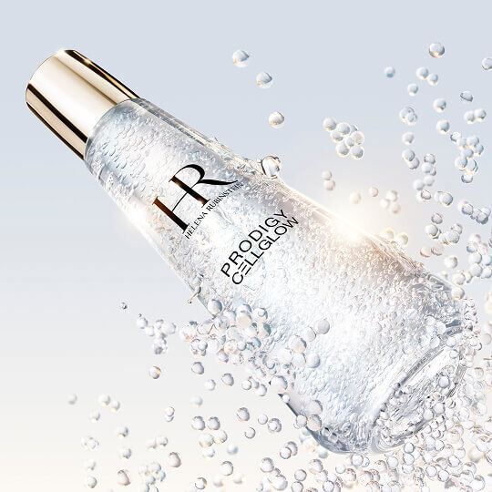 Helena Rubinstein Prodigy Cellglow Serumflasche, gefullt mit Blaschen, geneigt und umgeben von funkelnden schwebenden Blaschen, auf hellem und leuchtendem Hintergrund.