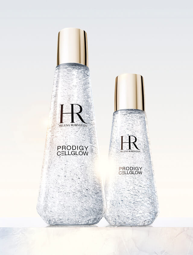  Zwei transparente Helena Rubinstein Prodigy Cellglow Serumflaschen, eine große und eine kleine, gefullt mit hydratisierenden Blaschen und goldenen Kappen, auf hellem Hintergrund.