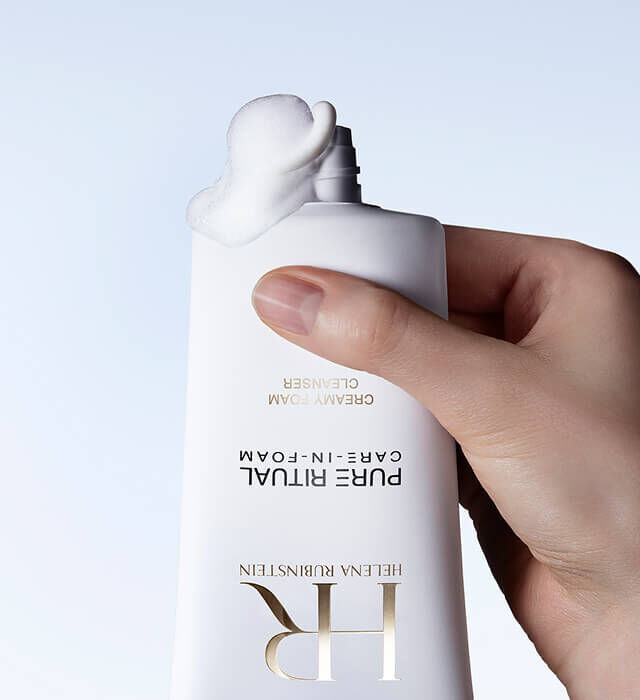 Eine Hand druckt auf eine Tube Pure Ritual Care-in-Foam von Helena Rubinstein, aus der eine kleine Menge des Produkts austritt.